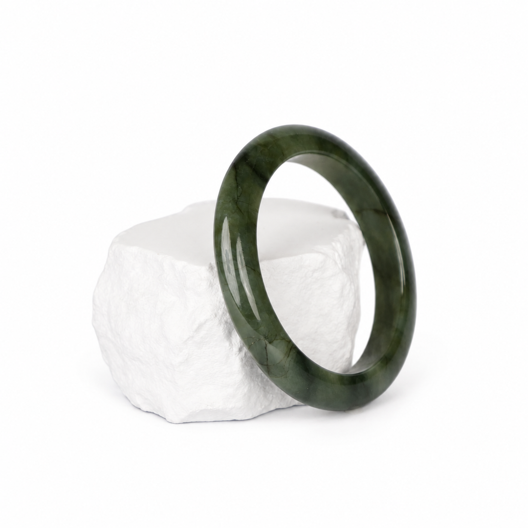 Dark green jadeite bangle on a white textured display block, three-quarter view
