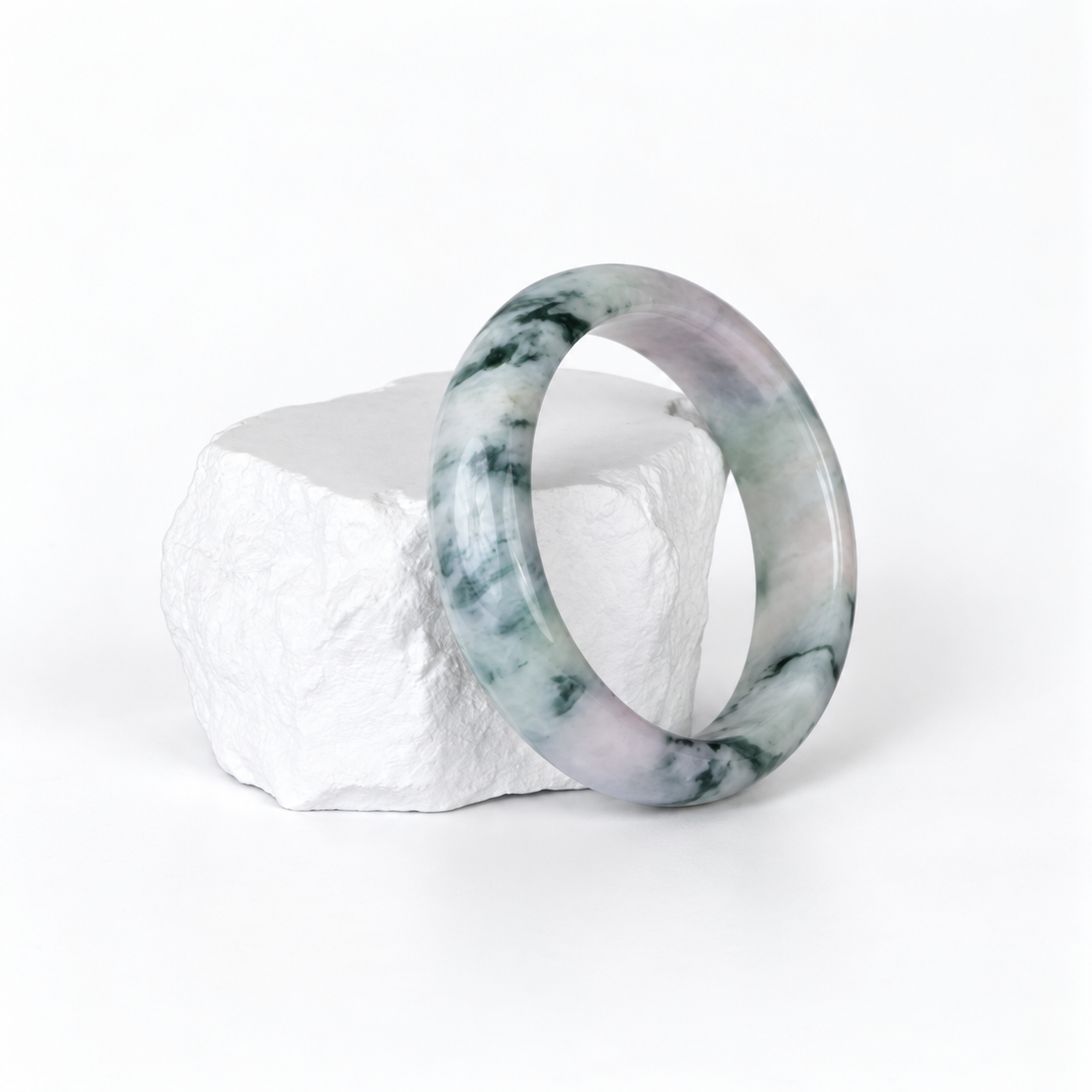 White and green moss-in-snow jadeite bangle on a white textured display rock, three-quarter view